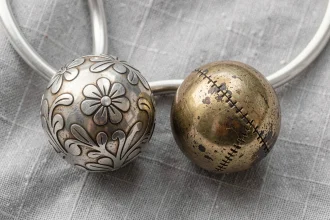 Comparaison entre une vraie bola de grossesse en argent et une contrefaçon posées sur un tissu en lin gris