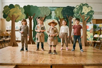 Groupe d'enfants en costumes faits main jouant Le Petit Poucet sur une scène d'école décorée de décors en carton peint